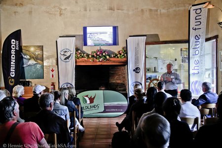 Voor links is Wilfred Chivell, stigter van Dyer Island Conservation Trust, besig om die gaste oor die agtergrond van die beplande African Penguin & Seabird Sanctuary in te lig, kort vóór die sooispit-seremonie